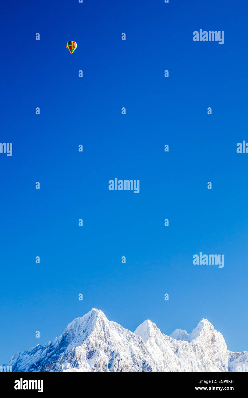 Ein Heißluft-Ballon-Segel über Schnee bedeckt Berggipfel Stockfoto