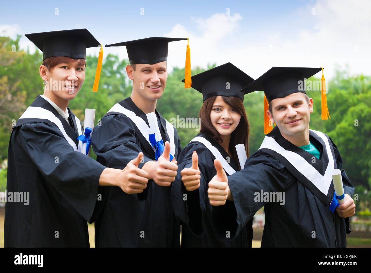 glückliche Schüler in Graduierung Kleider Diplome mit Daumen auftauchen Stockfoto