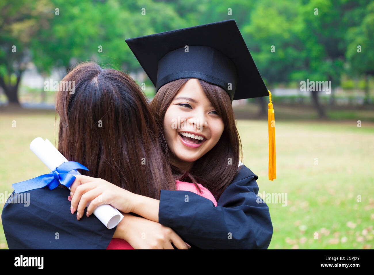 junge weibliche Absolventin umarmt ihre Freundin bei Abschlussfeier Stockfoto