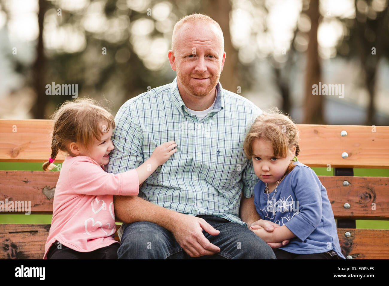 Vater mit zwei Töchtern, dass eineiige Zwillinge sind in einem Park in natürlichem Licht. Stockfoto