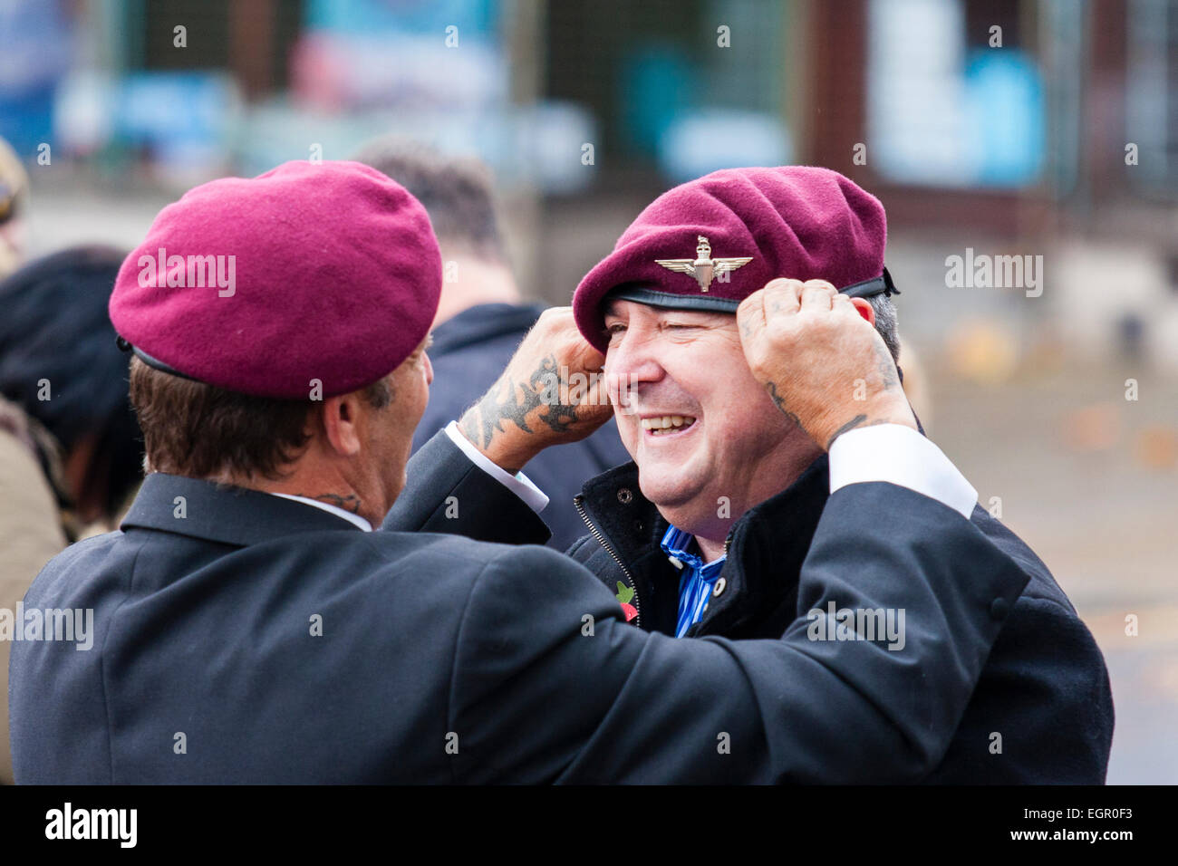 Zwei reife Männer, gekleidet in Jacken und Fallschirmjäger Baskenmütze, stehen draußen und plaudern bei einem Militärereignis. Einer passt die Baskenmütze des anderen an. Stockfoto