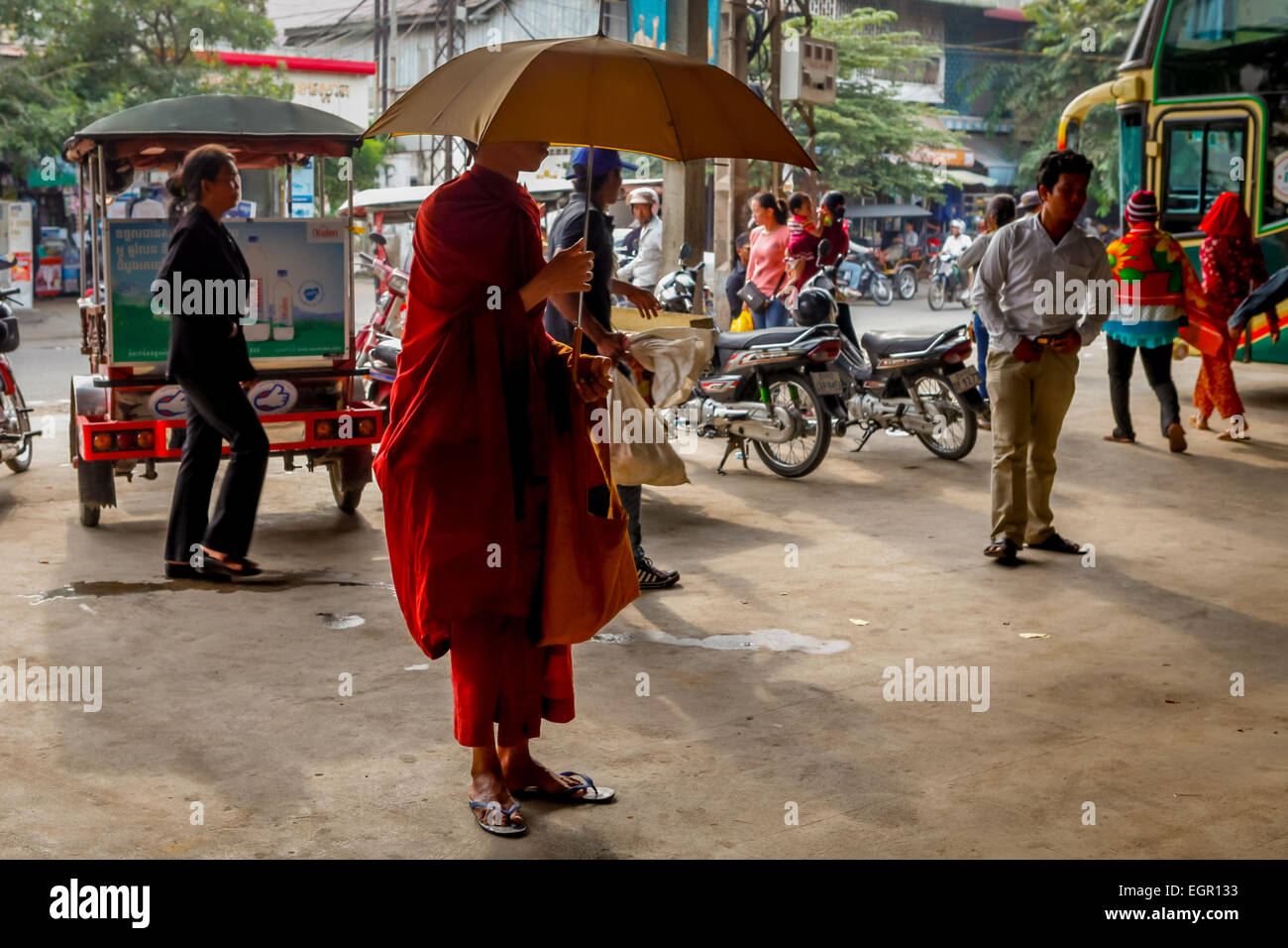 Ein buddhistischer Mönch, der einen Regenschirm trägt, während er während einer morgendlichen Almosenrunde an einer Intercity-Bushaltestelle in Phnom Penh, Kambodscha, steht. Stockfoto