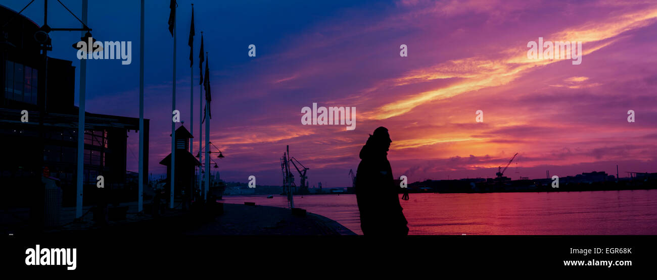 Ein Mann, Göta Älv und Göteborg Hafen unter einem dramatischen Sonnenuntergang blicken. Stockfoto