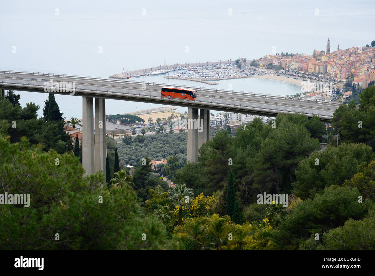 Sightseeing-Bus (mit Bewegungsunschärfen) auf einer Autobahnbrücke mit Blick auf die malerische Altstadt von Menton. Alpes-Maritimes, Französische Riviera, Frankreich. Stockfoto