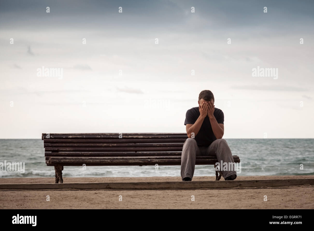 Trauriger Mann sitzt auf der alten Holzbank an der Meeresküste. Vintage getönten Foto mit Retro-toning Filterwirkung Stockfoto