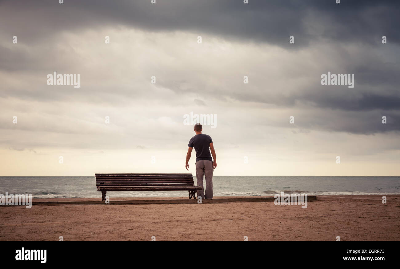Müder junger Mann geht auf der alten Holzbank an der Meeresküste. Vintage getönten Foto mit Retro-toning Filterwirkung Stockfoto