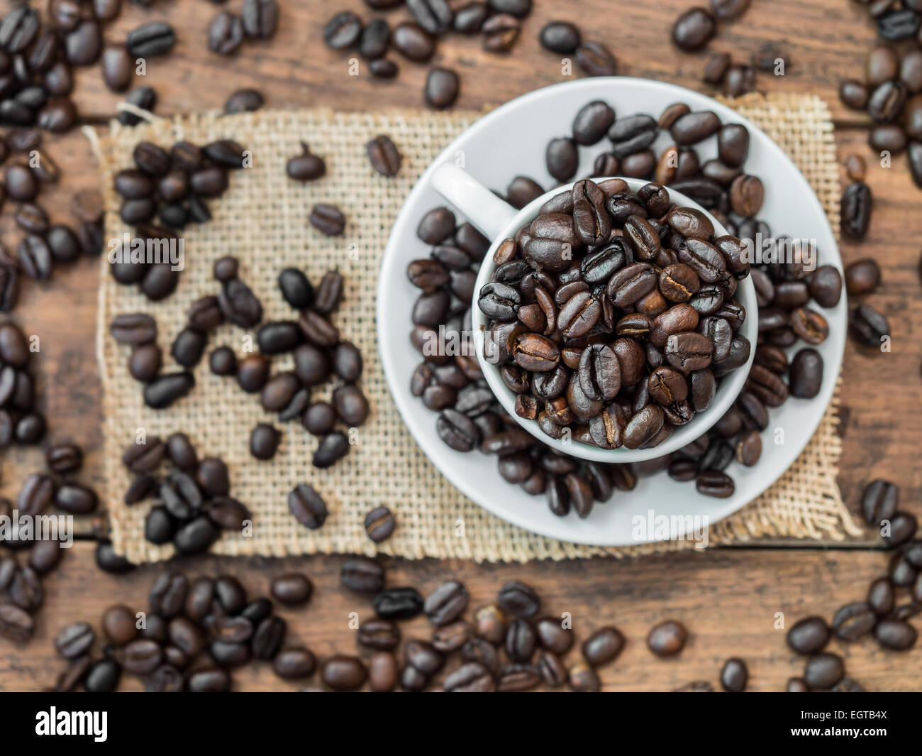 Weiße Espressotasse voll von gerösteten Kaffeebohnen auf einem hölzernen rustikalen Hintergrund. Horizontale Ausrichtung, Draufsicht. Stockfoto