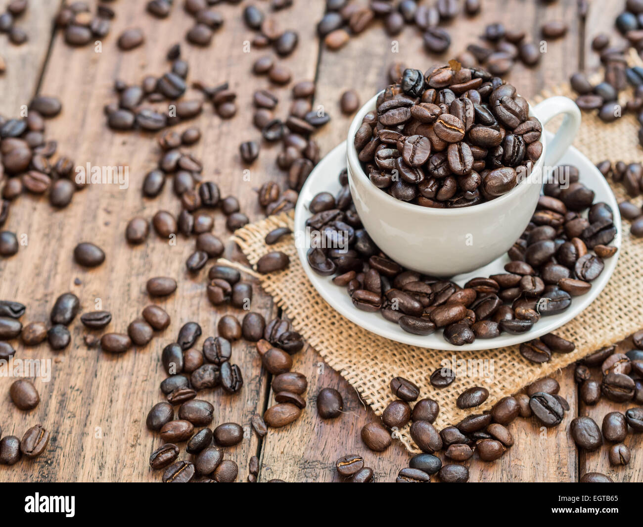Weiße Espressotasse voll von gerösteten Kaffeebohnen auf einem rustikalen Holztisch. Horizontal / Querformat. Hintergrund. Stockfoto