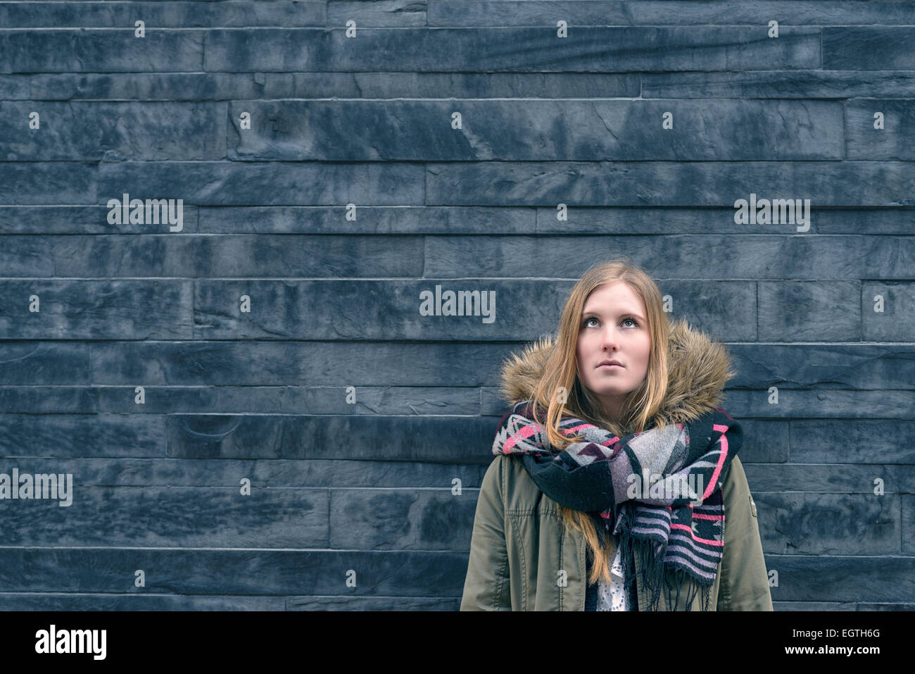 Trendige junge Studentin in warmen Winter Mode stehen denken oder Tagträumen gelehnt eine strukturierte graue Wand suchen Stockfoto