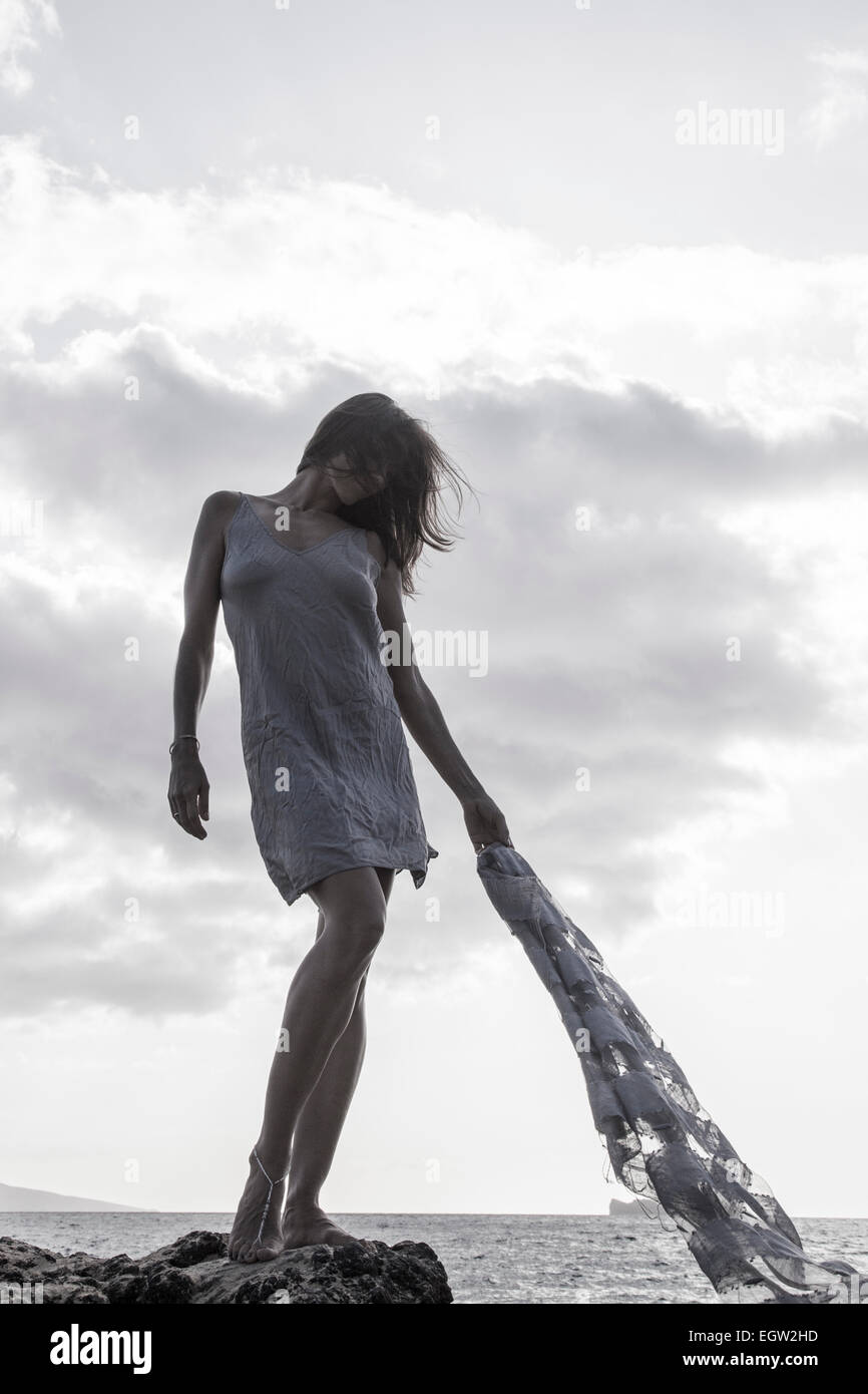 Frau stehend auf Felsen in der Nähe von Meer, Stoff im Wind zu halten. Stockfoto