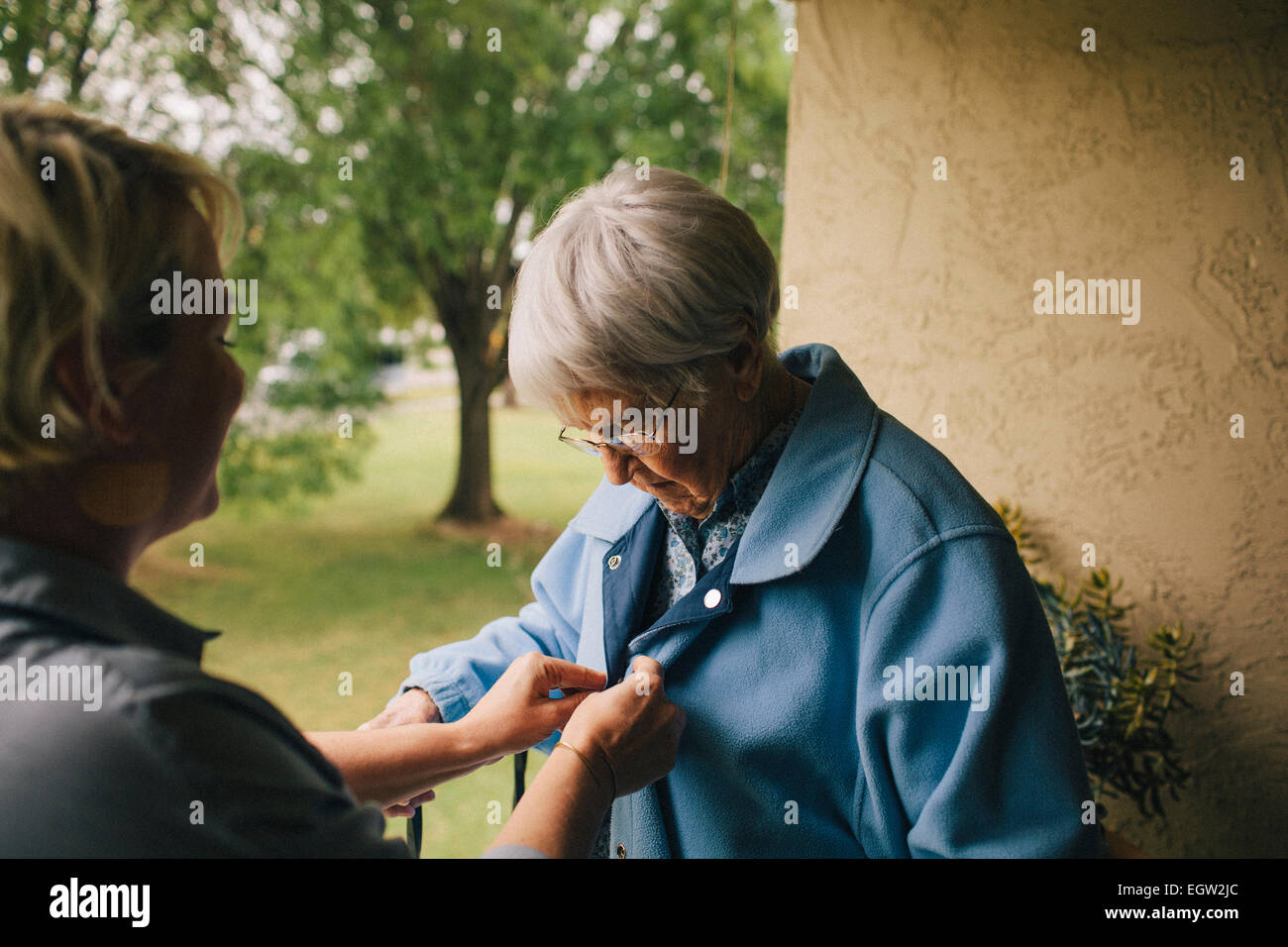 Jüngere Frau hilft senior Frau Knopf ihrer Jacke. Stockfoto