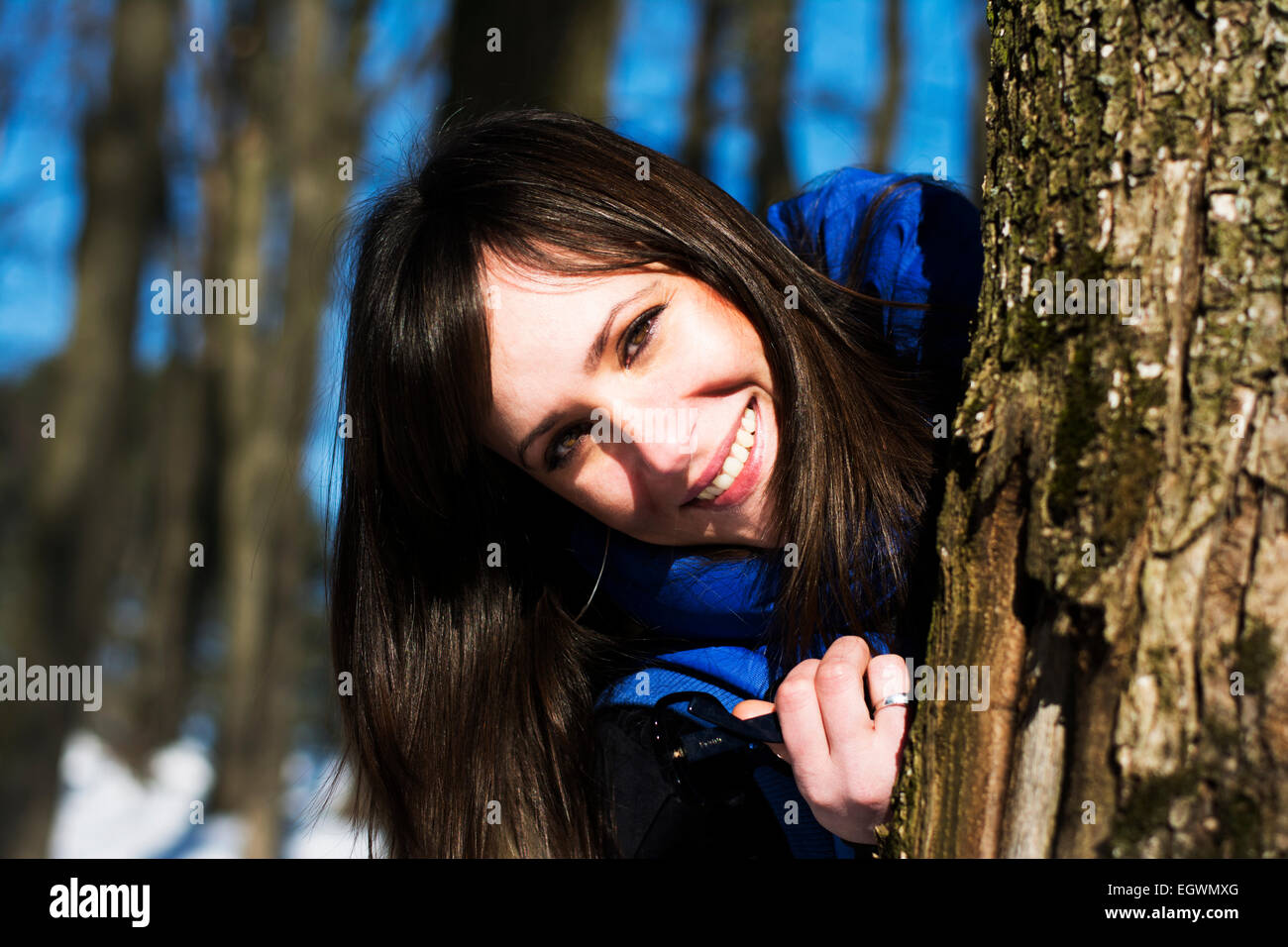 Hübsche Frau spähen hinter dem Baum im Wald Stockfoto