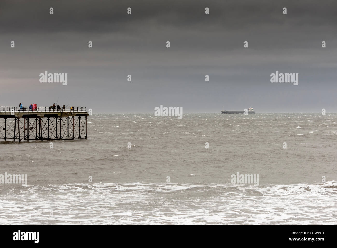 Saltburn Pier mit ein paar Wanderer und Leute Angeln. Ein Frachtschiff Fracht Schiff ist vor Anker am Horizont. Stockfoto