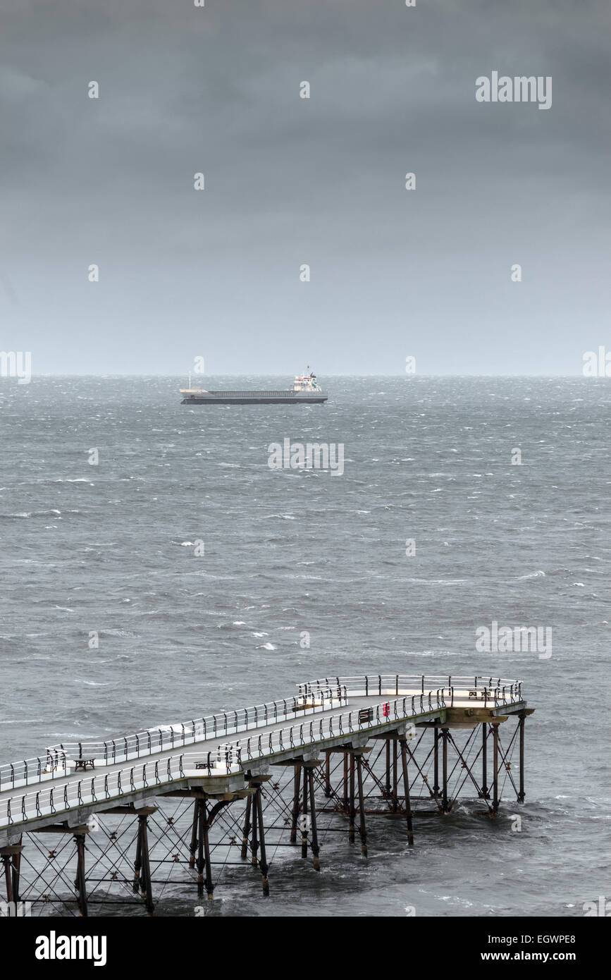Leere Saltburn-by-the-Sea-Pier mit einem Frachtschiff Fracht Schiff vor Anker hinaus unter einem düsteren Himmel Englands Nordseeküste Stockfoto
