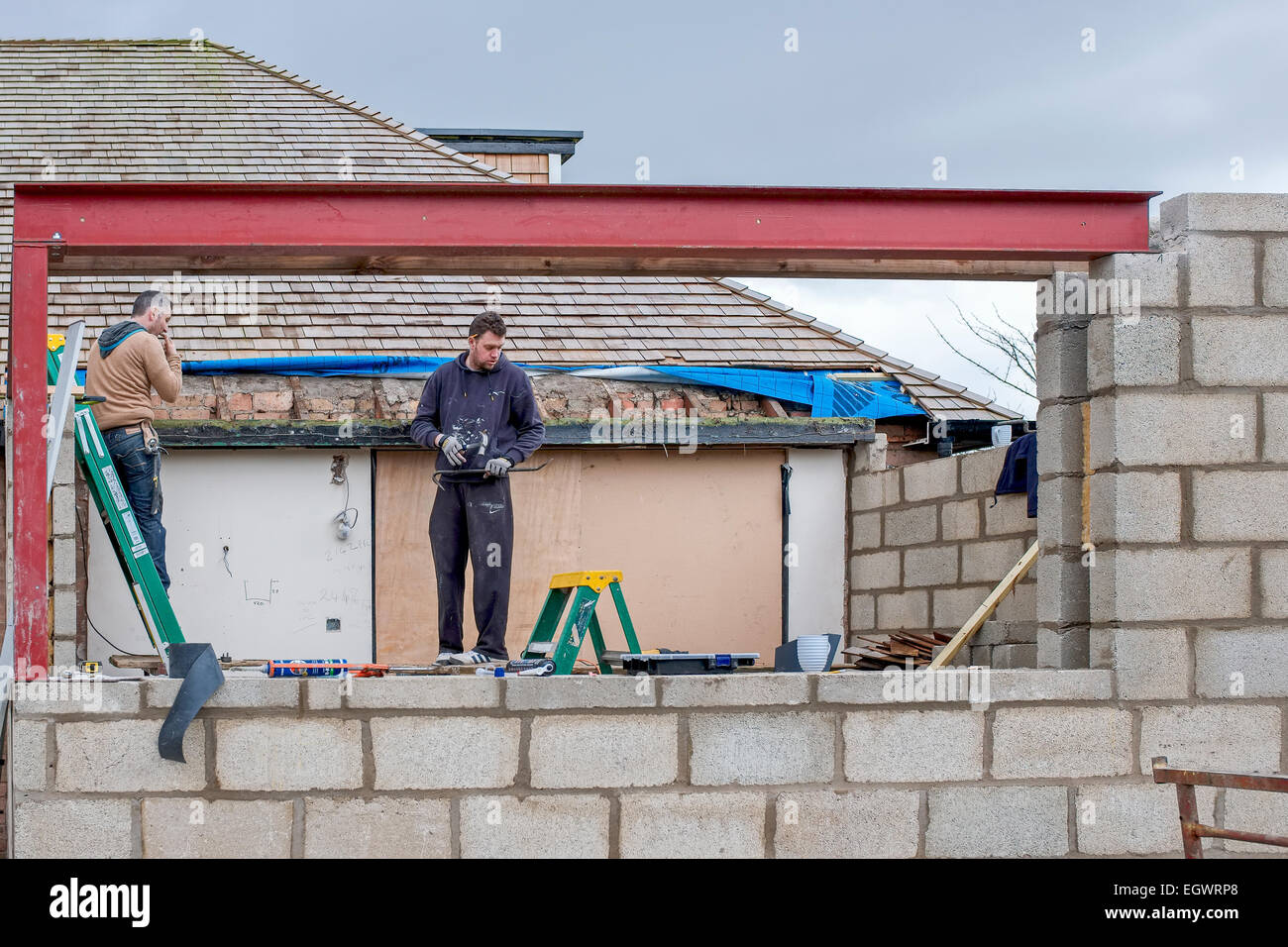 Zwei Arbeiter bauen eine Wohnhauserweiterung, Stand auf einer Plattform, Schuß durch eine Fensteröffnung mit roten Stahl Balken erstellt. Stockfoto