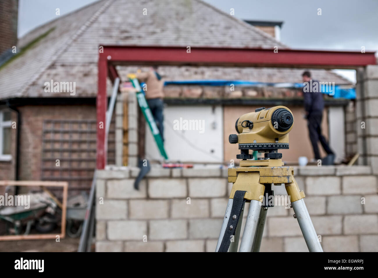 Theodolit auf einer Wohn Baustelle Erweiterungsbau ein Haus. Zwei Arbeiter sind im Hintergrund unscharf gestellt. Stockfoto