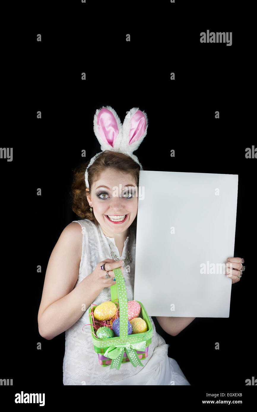 Junge Frau posiert mit Hasenohren, Osternest mit Pailletten Eiern und leere Zeichen für textfreiraum auf schwarzem Hintergrund. Stockfoto
