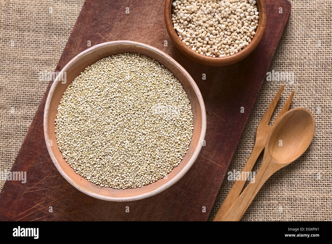 Obenliegende Aufnahme von rohen weißen Quinoa (Chenopodium Quinoa lat.) Getreide Samen in Schüssel mit geplatzten Quinoa Getreide auf Holzbrett Stockfoto