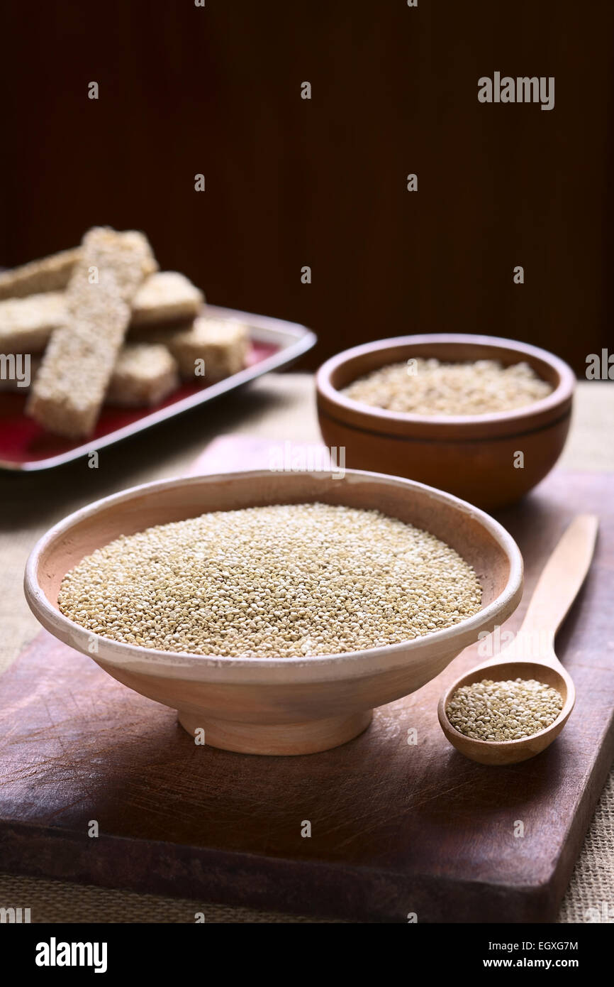 Roh weiß Quinoa (Chenopodium Quinoa lat.) Getreide Samen in Schüssel mit Quinoa Müsliriegel in den Rücken auf Holzbrett Stockfoto