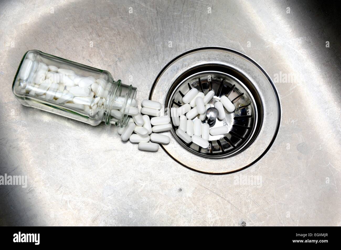 Ein Glas mit Tabletten verschütten heraus in ein Waschbecken Abfluss Stockfoto