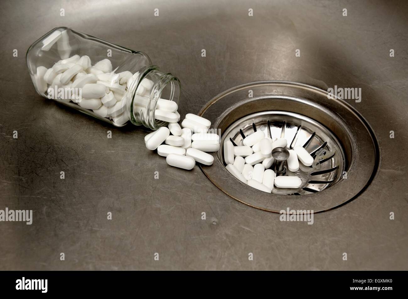 Ein Glas mit Tabletten verschütten heraus in ein Waschbecken Abfluss Stockfoto