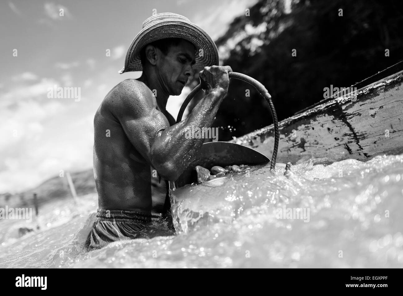 Ein kolumbianische Sand Bergmann entlädt einen Eimer voller Kies in seinem Boot verankert in der Mitte des Flusses in Cartago, Kolumbien. Stockfoto