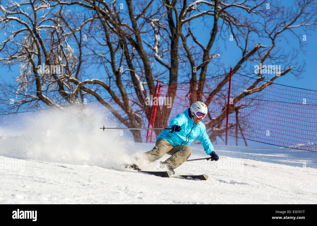 Skifahrer mit hoher Geschwindigkeit auf der Piste im weichen Schnee an einem sonnigen Tag auf einem Hintergrund von Bäumen und wolkenlosen blauen Himmel. Geringe Schärfentiefe Stockfoto