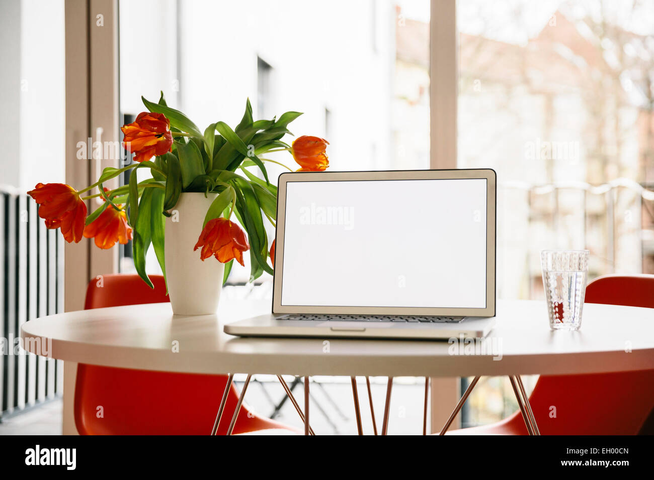 Laptop-Bildschirm auf einem weißen runden Tisch mit roten Tulpen und Stühlen Stockfoto