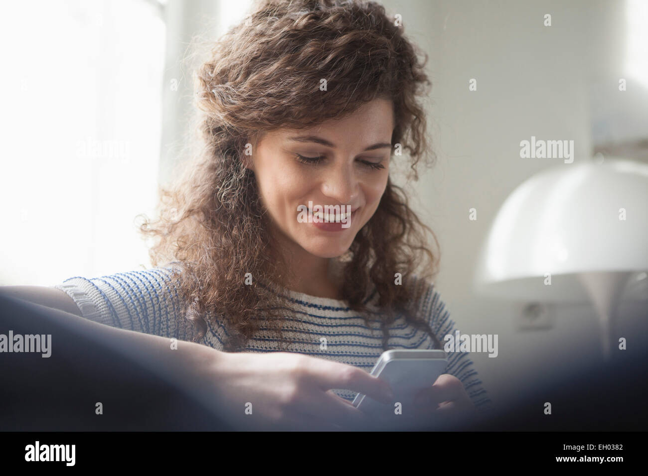 Junge Frau zu Hause mit Blick auf Handy Stockfoto