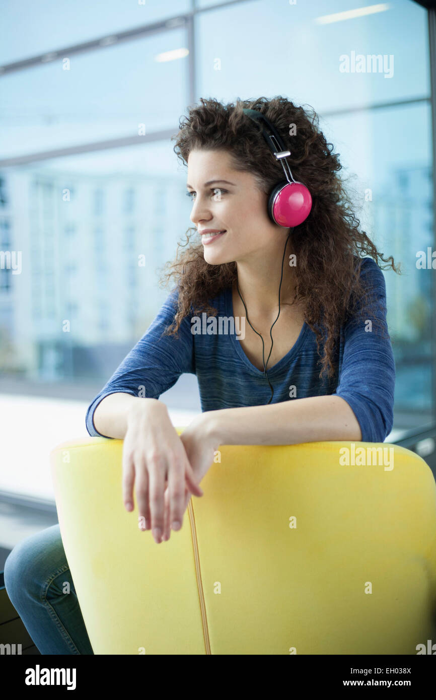 Lächelnde junge Frau mit Kopfhörern am Fenster Stockfoto