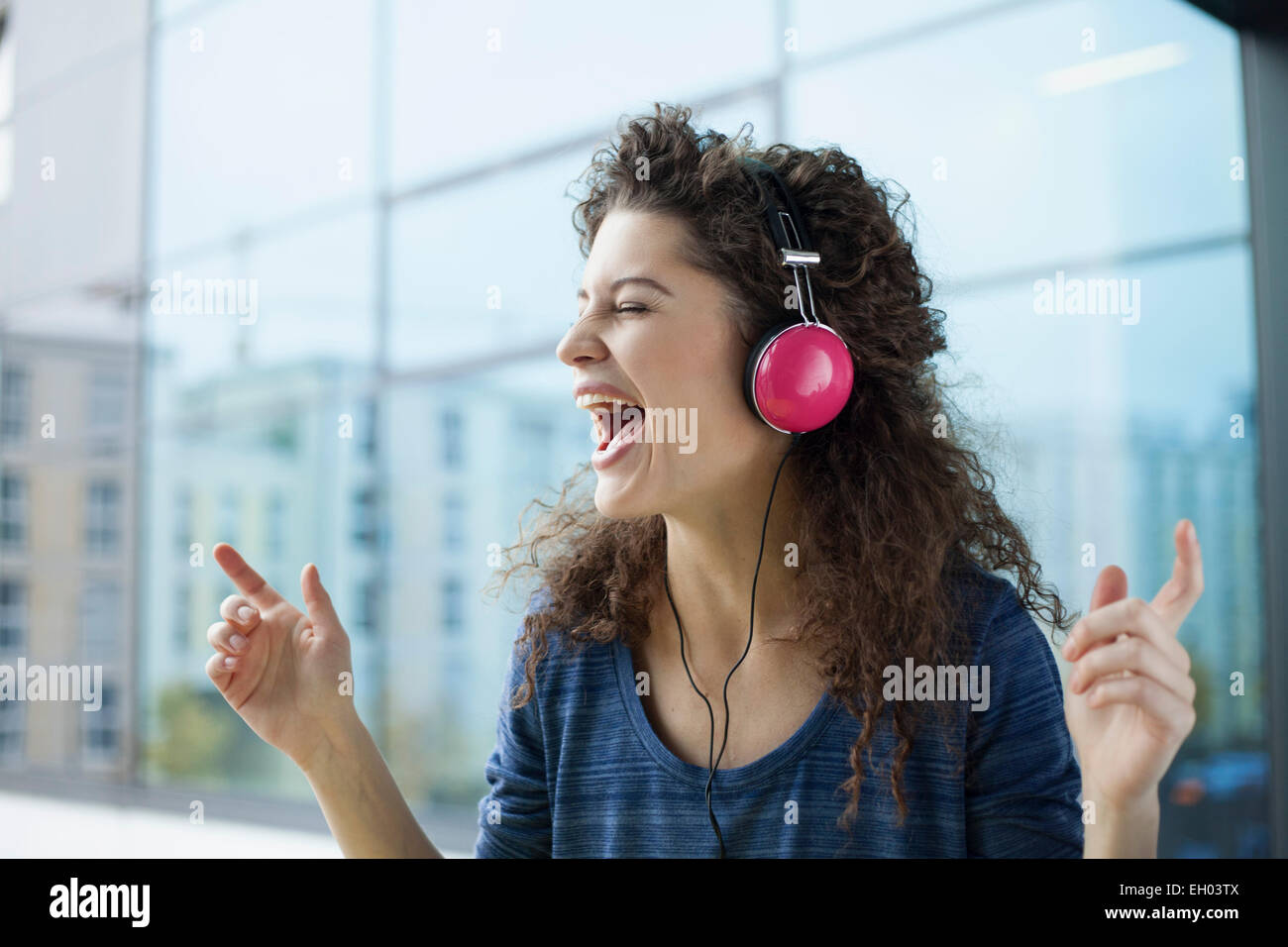 Junge Frau mit Kopfhörern am Fenster schreien Stockfoto
