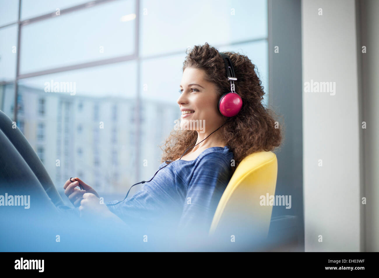Lächelnde junge Frau mit Kopfhörern am Fenster Stockfoto
