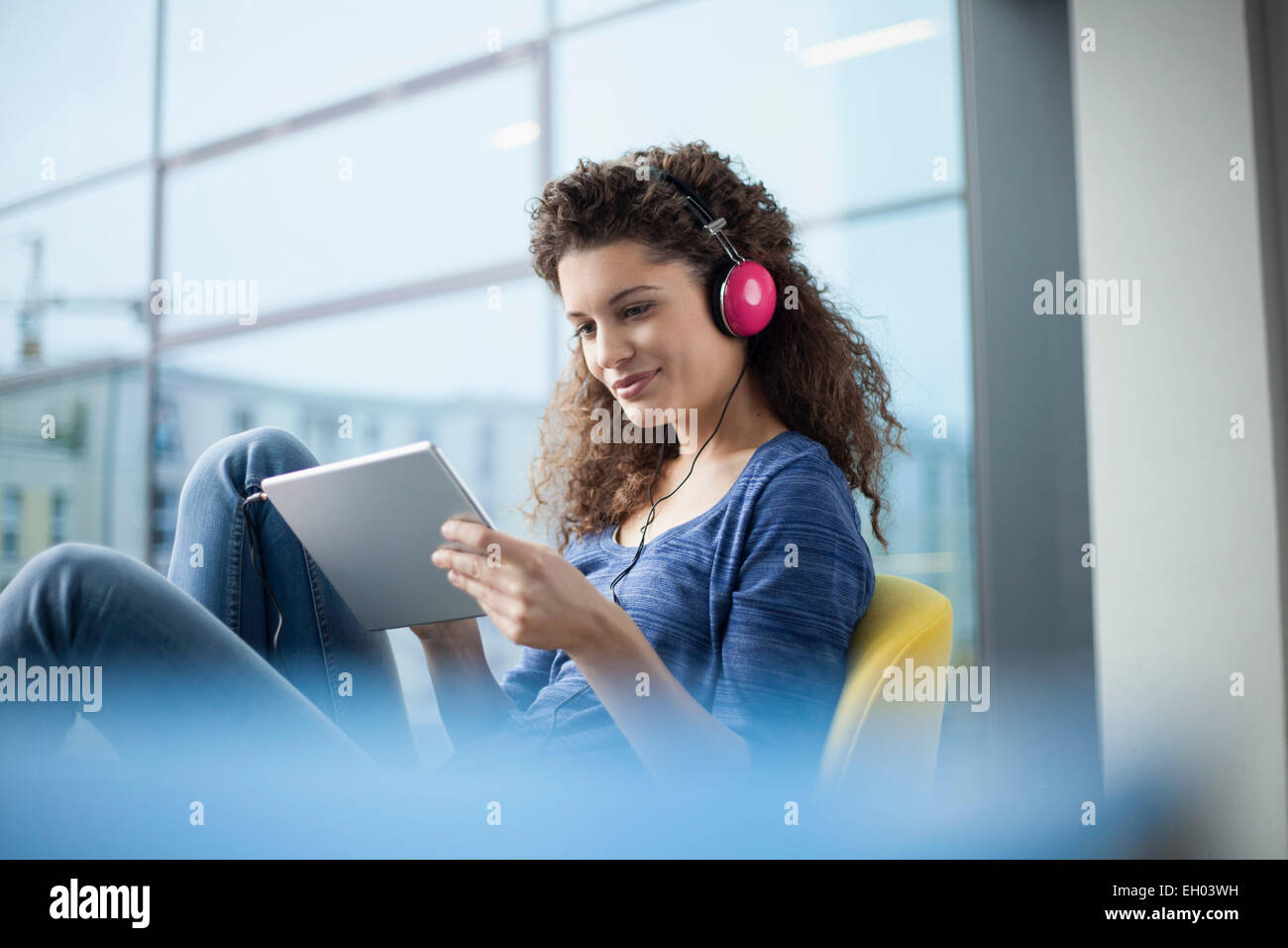 Lächelnde junge Frau tragen von Kopfhörern und mit digital-Tablette am Fenster Stockfoto