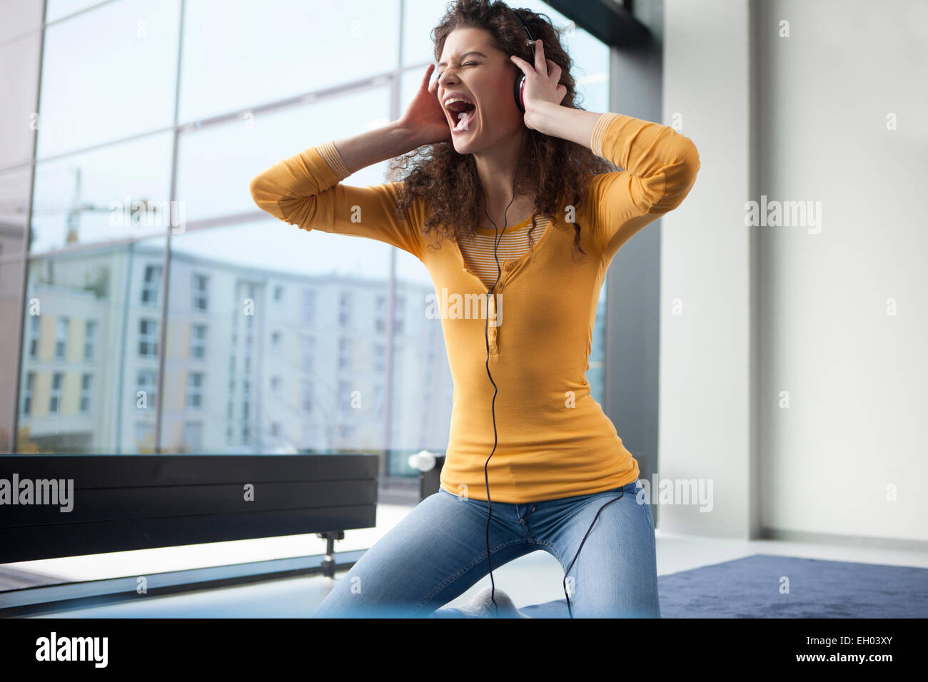 Junge Frau mit Kopfhörern am Fenster schreien Stockfoto