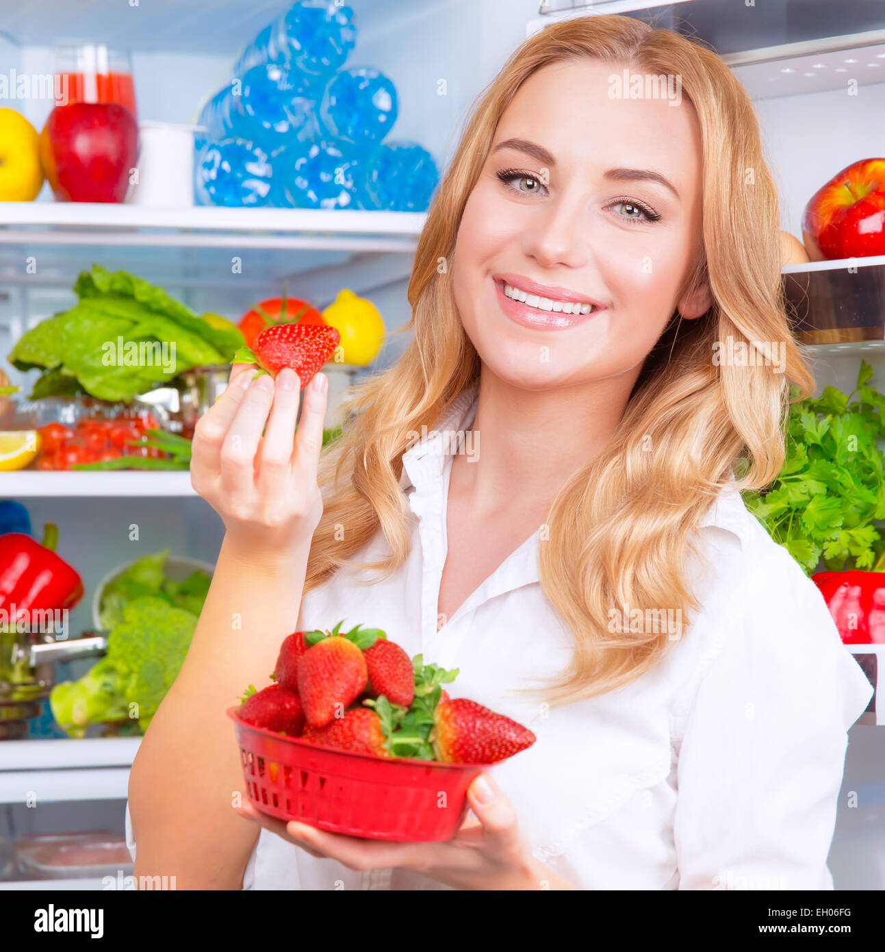 Closeup Portrait von schönen weiblichen Essen Erdbeere, offenen Kühlschrank voll mit Obst und Gemüse, Diät und gesunde Ernährung Stockfoto