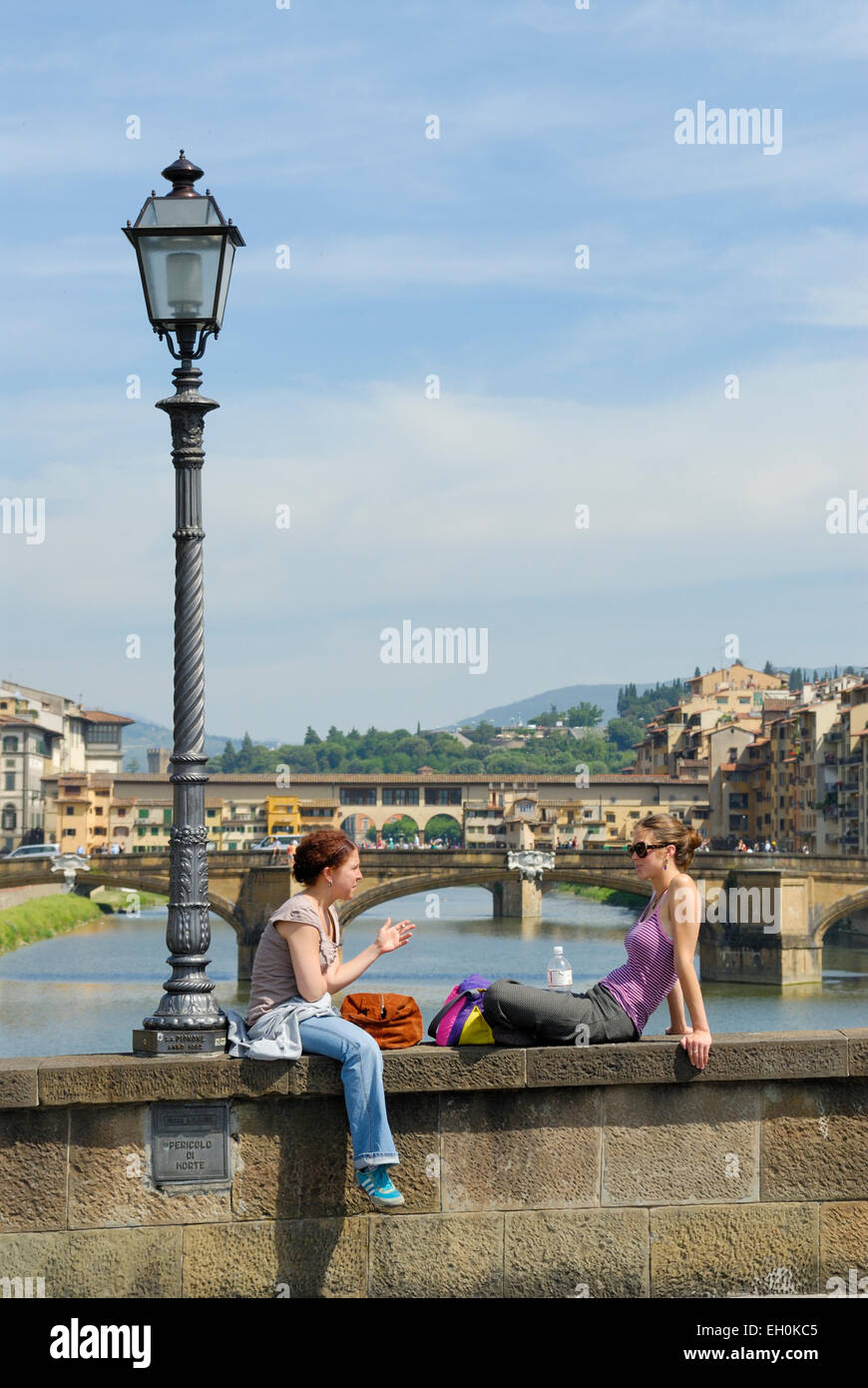 Touristen, die entspannend auf die Brücke Ponte Vecchio im Hintergrund - eine berühmte Brücke über den Fluss Arno, Florenz, Toskana, Italien Stockfoto