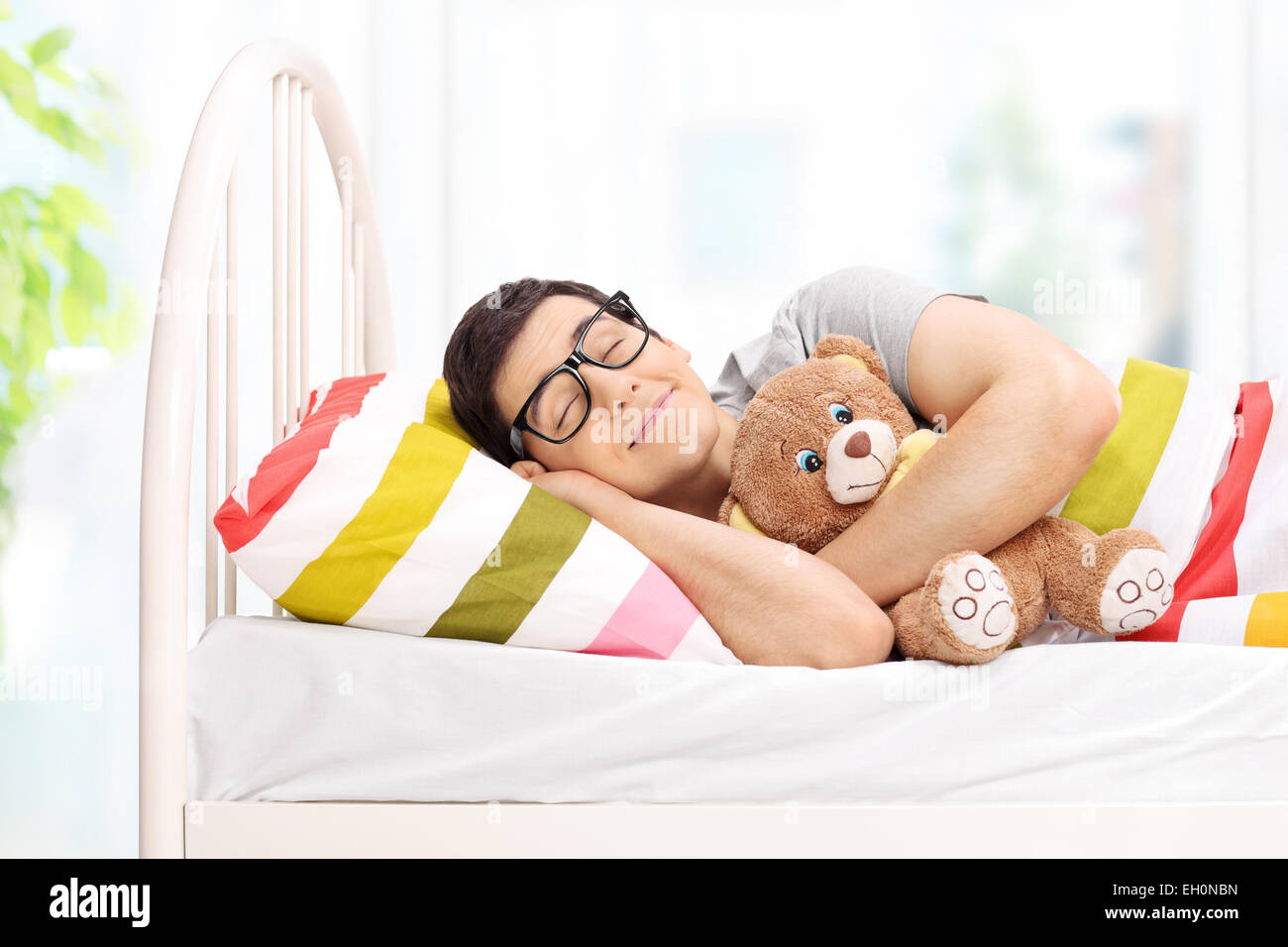 Kindisch junger Mann mit einem Teddy Bären zu Hause schlafen Stockfoto