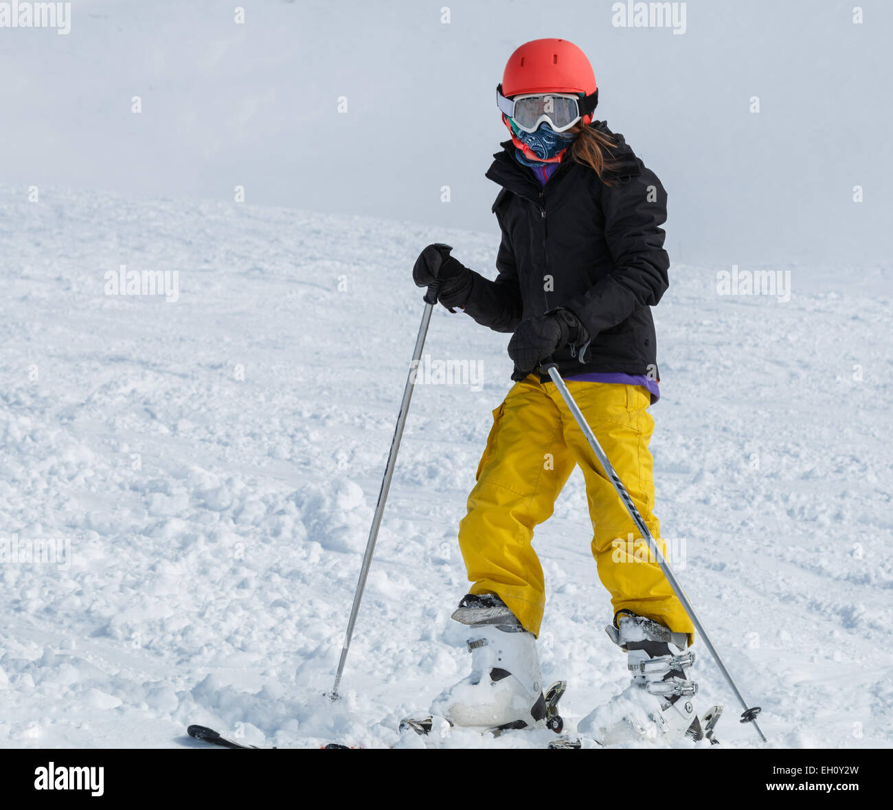 Junges Mädchen (9-11) Skifahren in leuchtend gelben Hose mit orange Helm Stockfoto