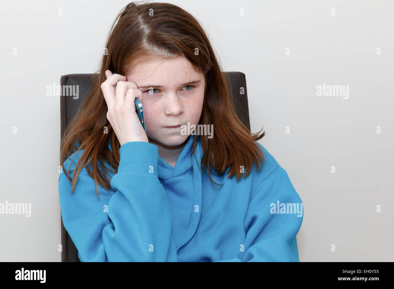 Mädchen (9-11 Jahre) mit rot-braunen Haaren und Sommersprossen reden über ein Handy mit einem Stirnrunzeln Kreuz oder wütenden Ausdruck. Stockfoto