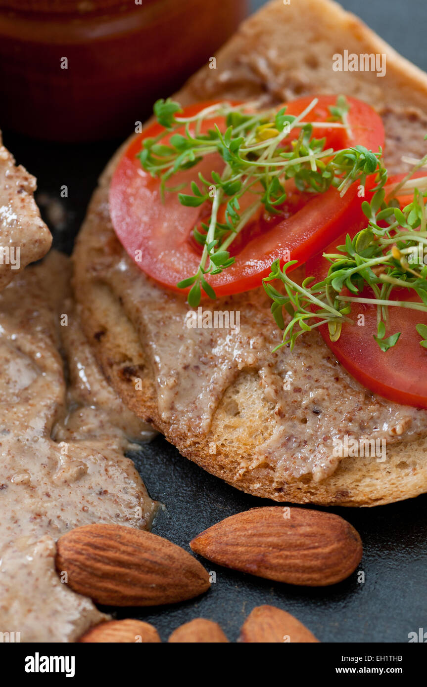 Hausgemachte Bio-Mandel-Butter auf Brot mit Tomaten und Kresse. Stockfoto