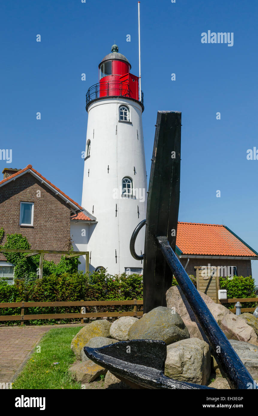 Weißer und roter Leuchtturm von Urk mit front in einen großen schwarzen Anker und einige Felsbrocken Stockfoto