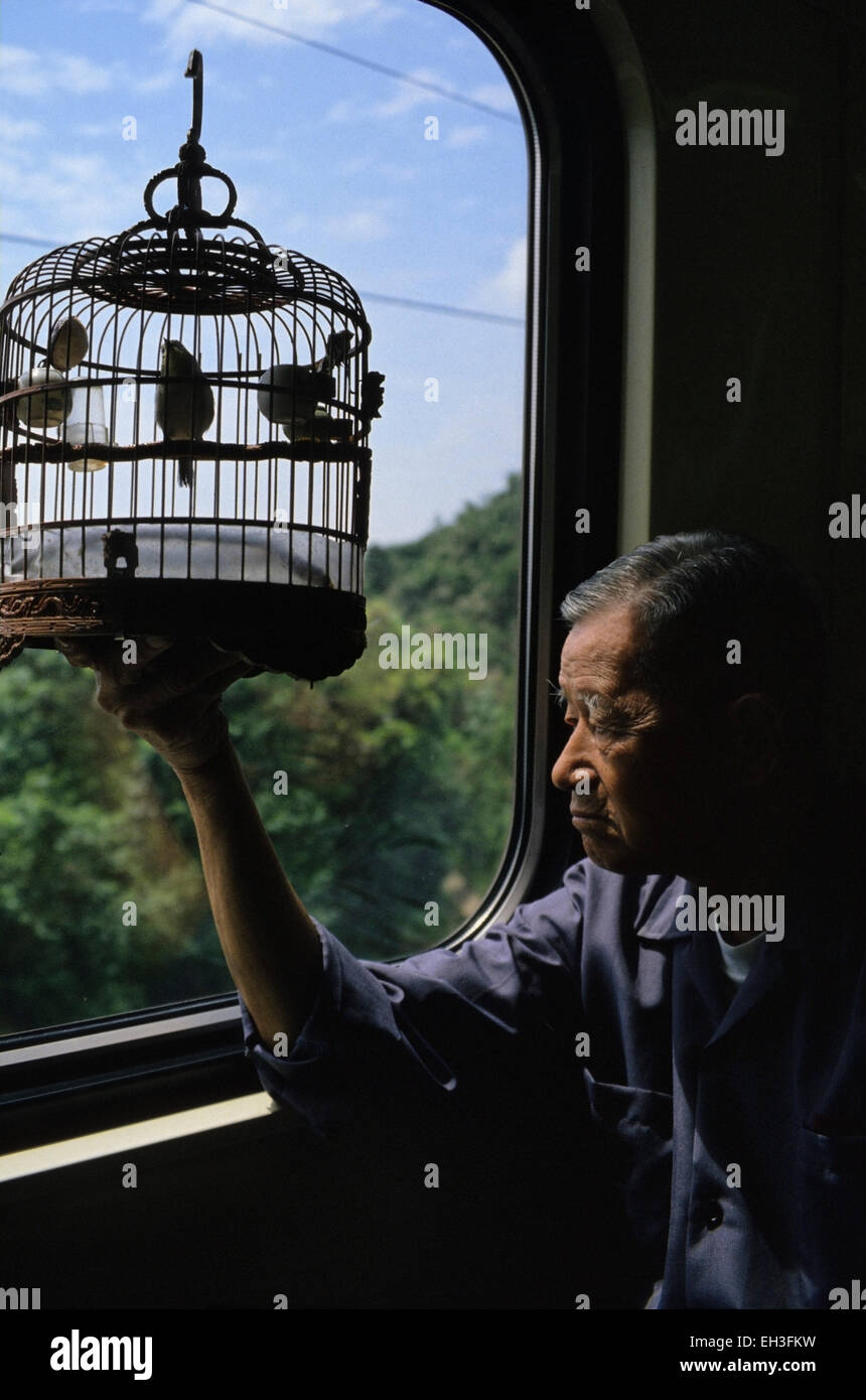 Alter Mann mit Vogel singen im Käfig an Bord Zug, Singapur Stockfoto