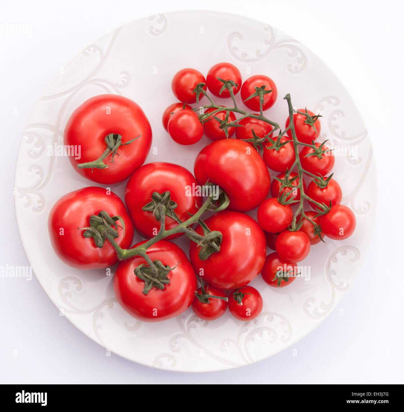 Großen Fleischtomaten mit kleiner Piccolo Kirschtomaten am Rebstock auf einem weißen Teller. Stockfoto