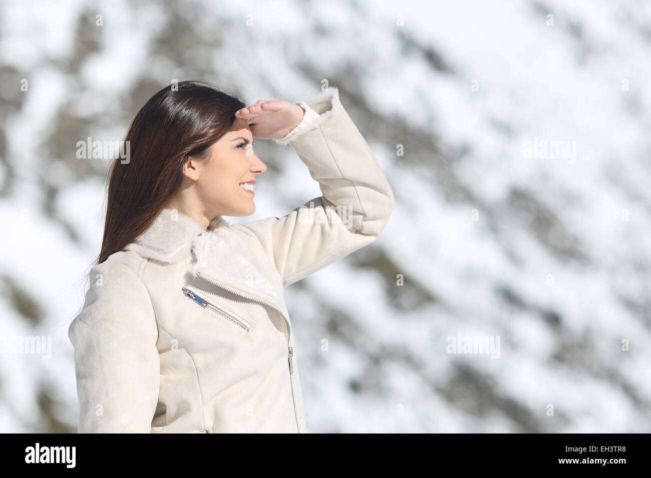 Frau, ich freue mich mit der Hand auf der Stirn im Winterurlaub mit einem schneebedeckten Berg im Hintergrund Stockfoto
