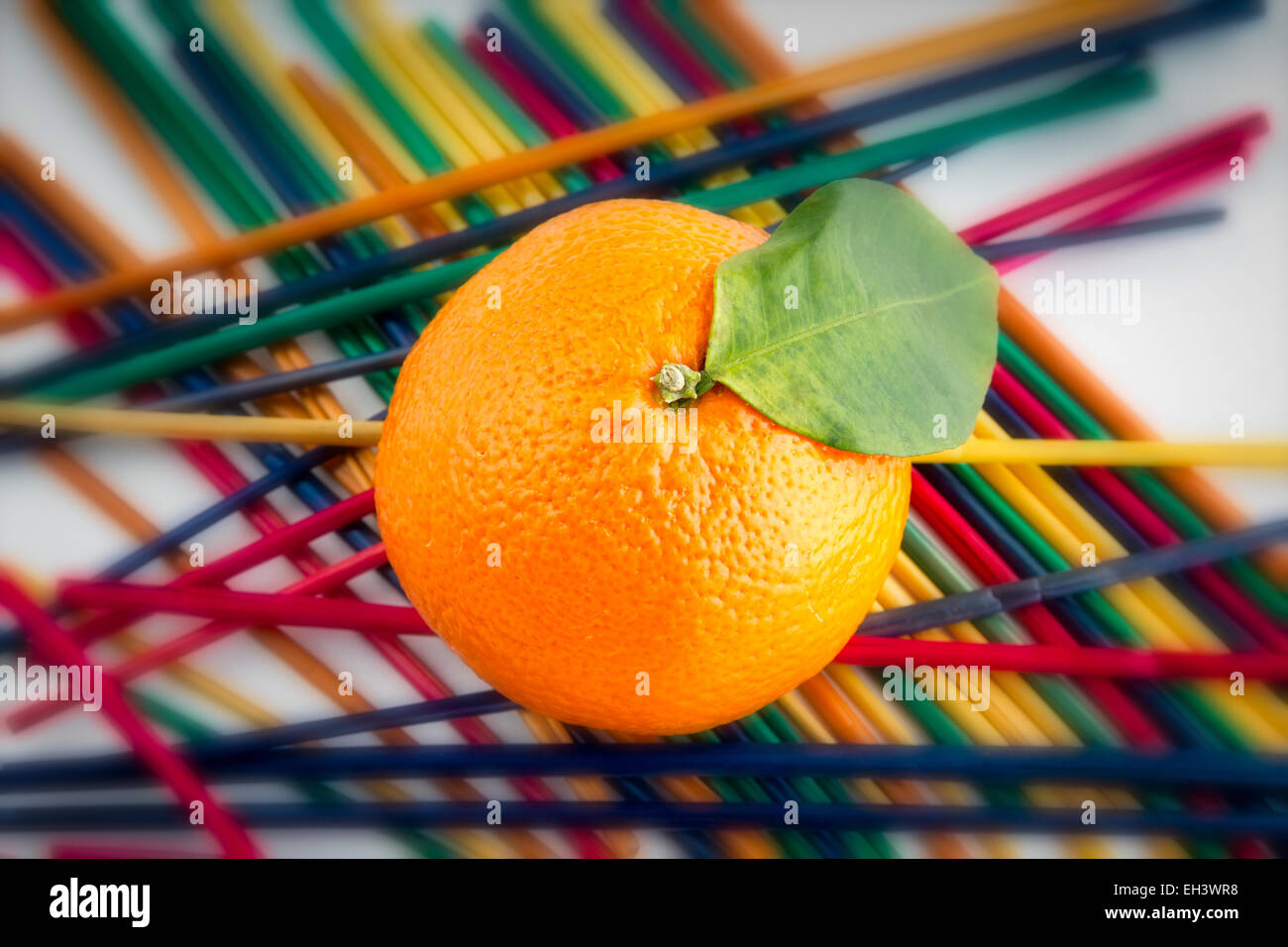 Einzelne Mandarin auf einem Raster von farbigen Strohhalme Stockfoto