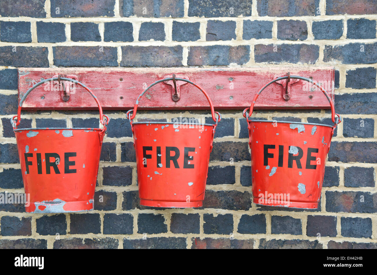 Drei rote Feuer Eimer hängen gegen eine Mauer Stockfoto