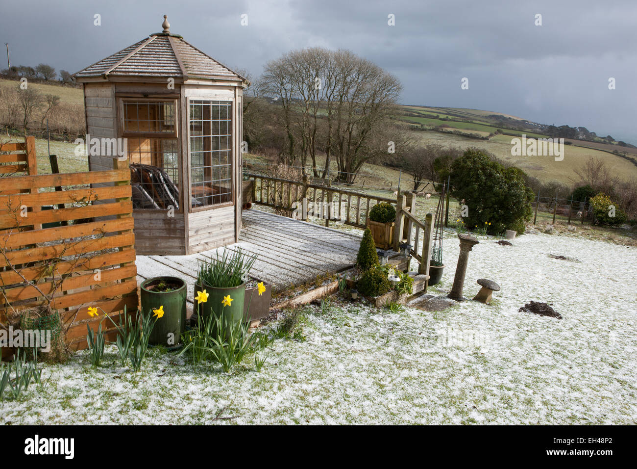 Ungewöhnliche Wetter für März in Cornwall, deckt ein Rückgang von Schnee, der Rasen und der Belag rund um das Gartenhaus. Stockfoto