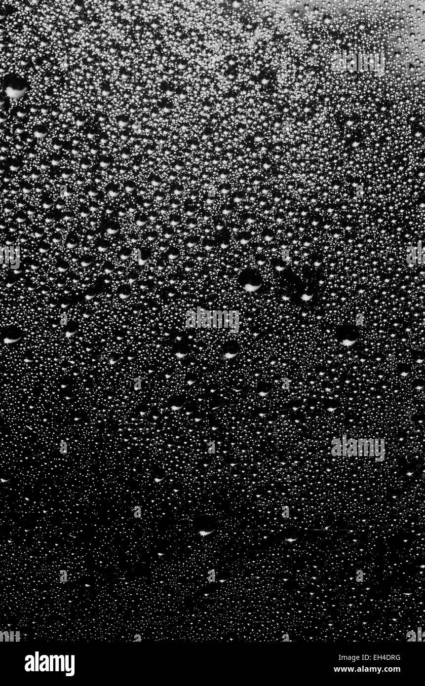 Gruppe von Tropfen mit verschiedenen Dimensionen auf einer Oberfläche in schwarz und weiß als Hintergrund Stockfoto