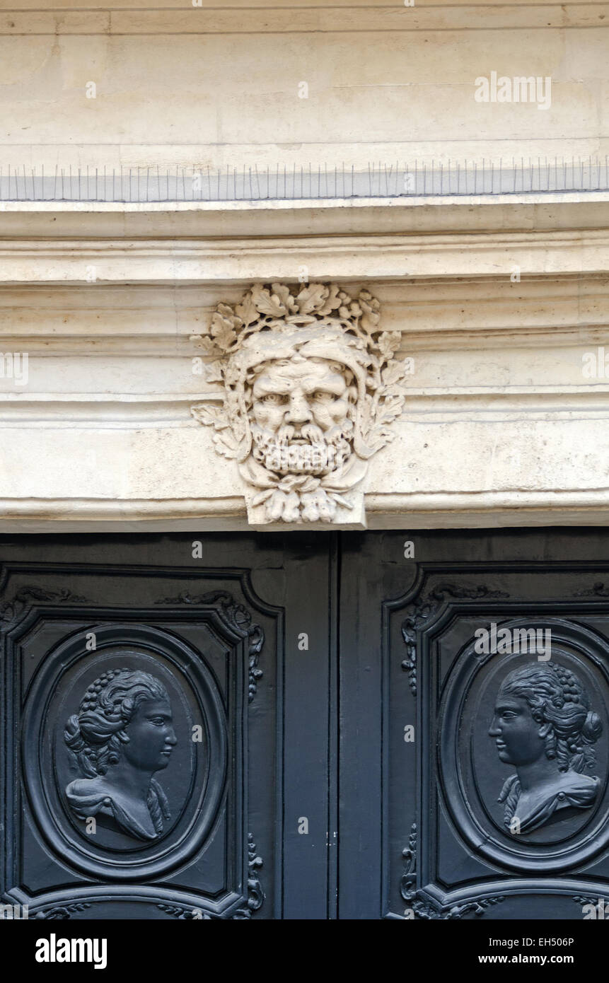 Eine ausdrücklich geschnitzte Gesicht bewacht eine Tür, dekoriert mit Cameo-Stil Porträts, Rue de Vielle du Temple, Paris. Stockfoto