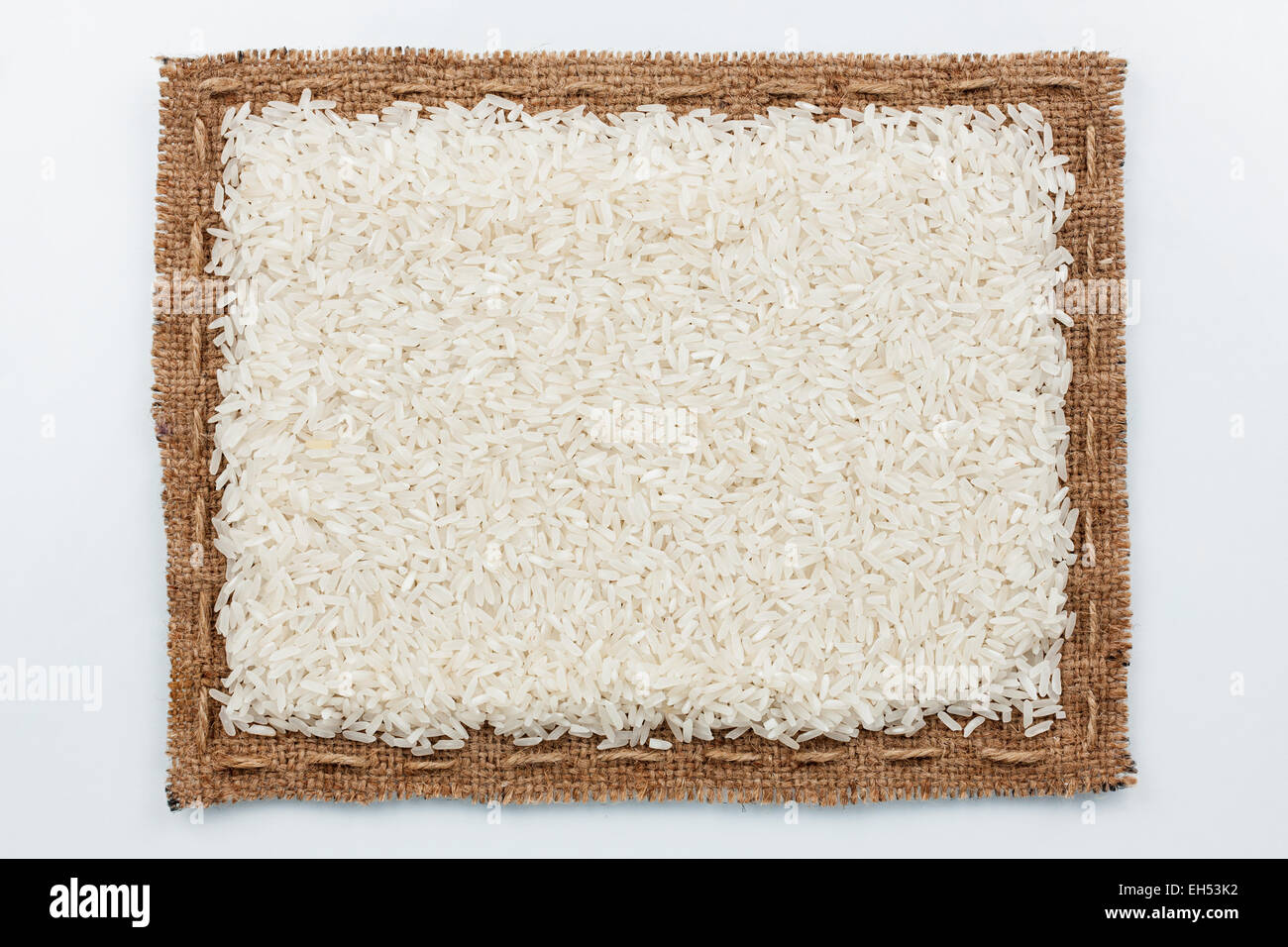 Rahmen von Sackleinen und Reis Getreide, liegend auf einem weißen Hintergrund Stockfoto